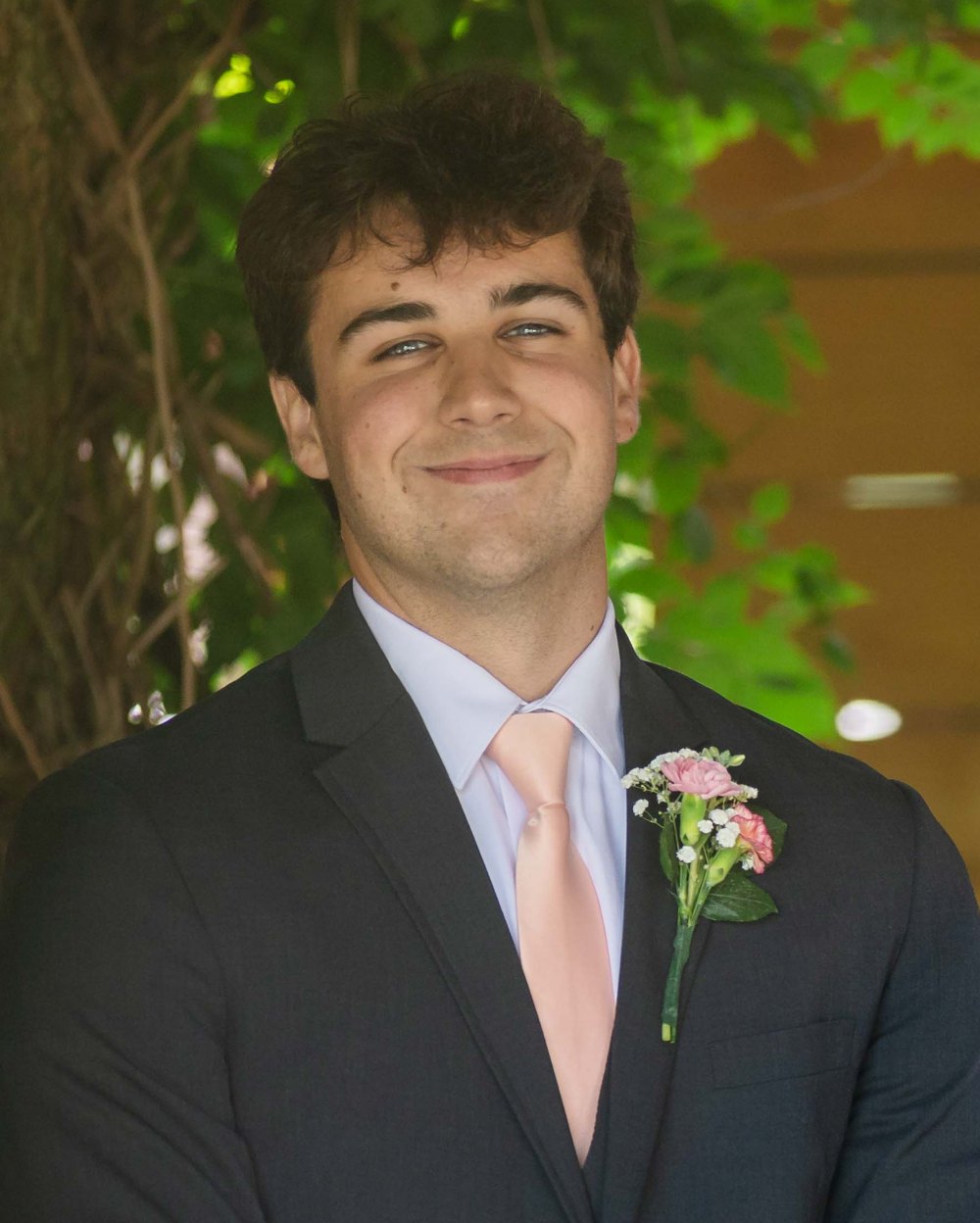 Billy Carlisle smiling in a navy suit with a pink tie and boutonniere