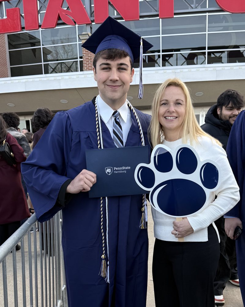 Billy in cap and gown at his Penn State Harrisburg graduation, holding his diploma cover, with his mother